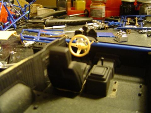 1979 Ford Bronco - The interior of a model vehicle is shown, with various parts and tools scattered around the workbench.