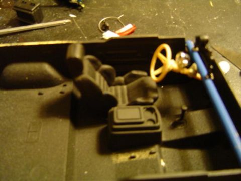 1979 Ford Bronco - Blurry overhead shot of a plastic scale-model truck interior tub sitting on a scratched workbench, with molded black bucket seats, center c…