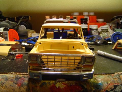 1979 Ford Bronco - Head-on view of an unpainted tan plastic scale model truck body under construction, with chrome grille surround, rectangular headlight beze…