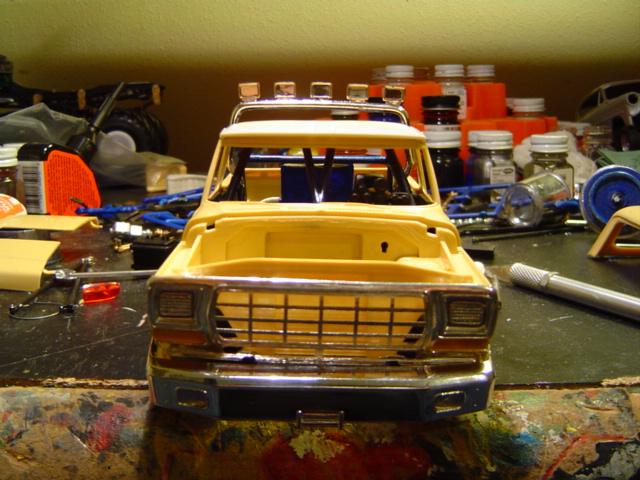 Front view of a tan plastic scale model truck body with chrome grille on a modeling bench