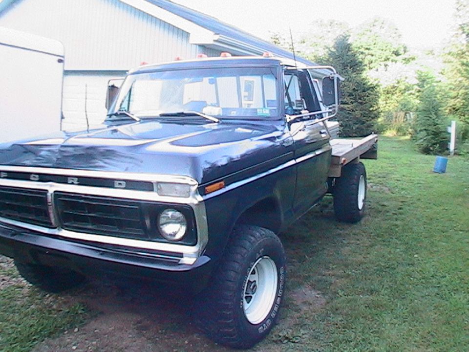 Black 1970s Ford flatbed 4x4 truck parked on grass by a shed