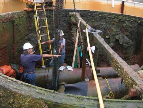 1988 Ford Bronco - Workers are seen lowering torpedoes into a large, rusty, and wet structure, possibly during a salvage or recovery operation.