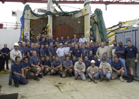 1988 Ford Bronco - A large group of people, mostly men in blue shirts, are gathered on a deck in front of industrial equipment.