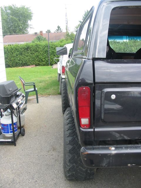 1985 Ford Bronco - A black Ford Bronco is parked in a driveway next to a white truck, with a grill visible on the left.