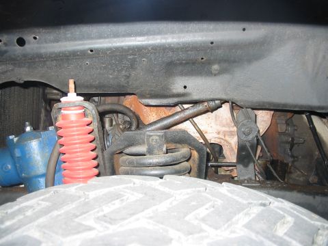 1985 Ford Bronco - Close-up view of the front suspension system, including a red shock absorber and steering components.