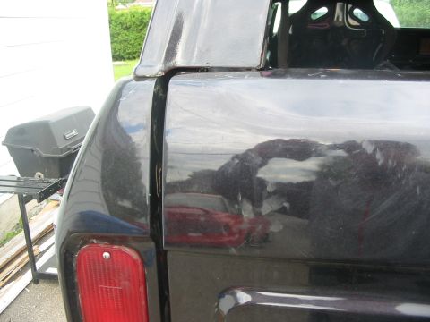1985 Ford Bronco - The rear quarter panel of a black SUV is visible, reflecting a red car in the background.