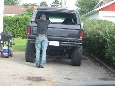1985 Ford Bronco - A person stands by the rear of a lifted black Ford Bronco, looking into the open window.
