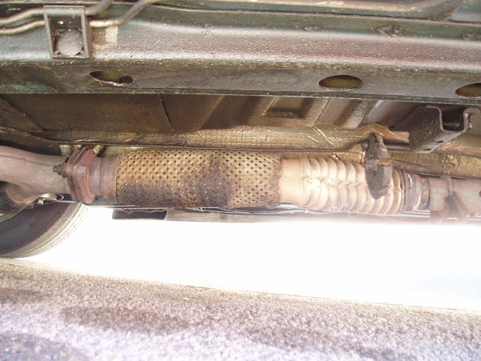 Underside view of a car's exhaust system, showing a flexible pipe and muffler section
