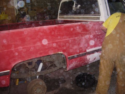 1981 Chevrolet C/K Pickup - Side view of a red pickup truck bed, undergoing repairs with the rear wheel off.