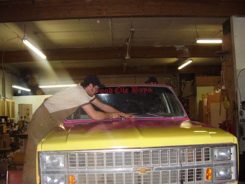 1981 Chevrolet C/K Pickup - A man works on the hood of a yellow and pink pickup truck inside a garage. The windshield has a decal that reads 'Good Ole Boys'.