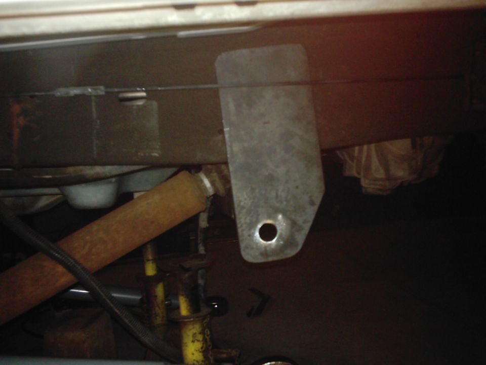 Close-up of a metal bracket with a hole, attached to a vehicle frame. Rusty pipe visible