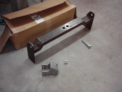 1978 Ford Bronco - A metal bracket and bolt are shown on a concrete floor, next to a partially opened cardboard box.