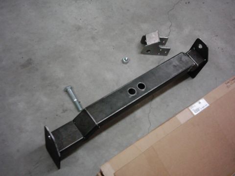 1978 Ford Bronco - A metal frame part, possibly for a vehicle, lies on a concrete surface with hardware and a box.