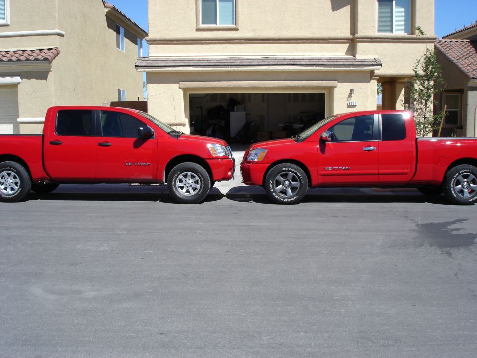 Two red Nissan Titan V8 pickups parked nose to nose in front of a house