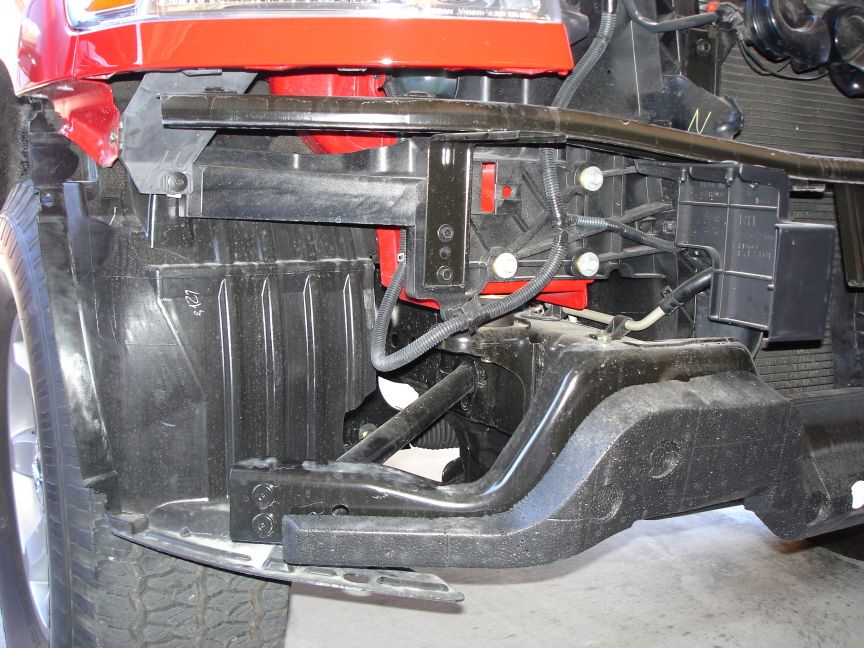Red pickup front corner stripped to the frame horn and black inner fender liner in a shop