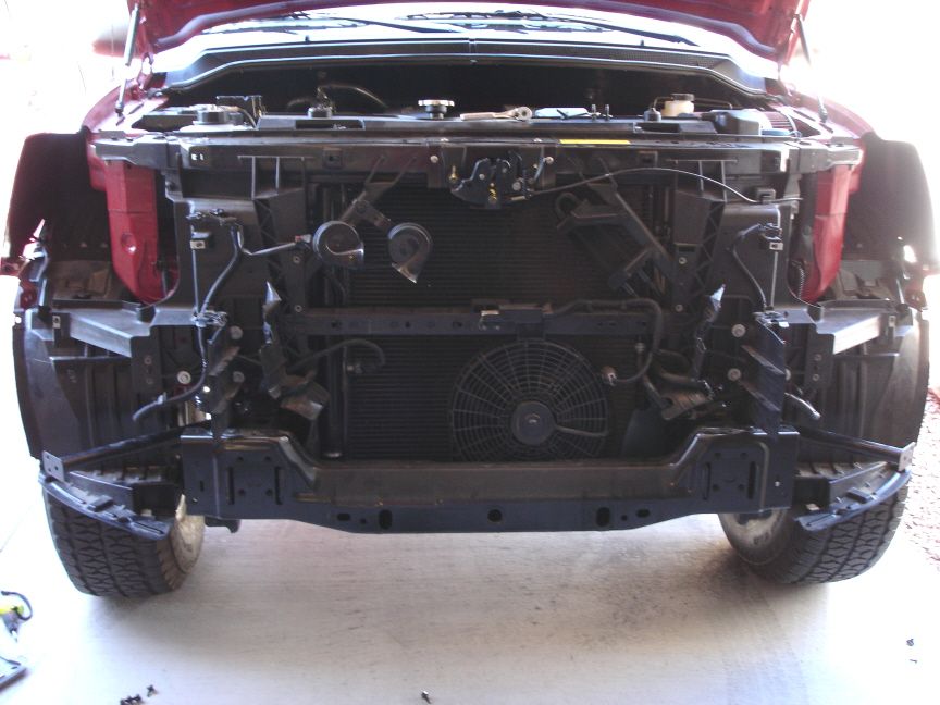 Red pickup with front bumper and grille removed exposing brackets and radiator