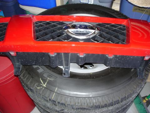 2005 Nissan Titan - A red Nissan grille with a chrome emblem is shown, resting on a tire.