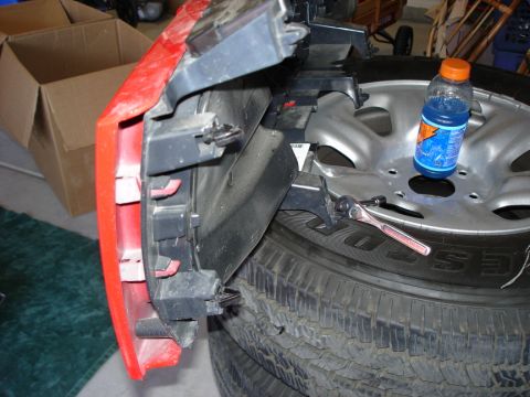 2005 Nissan Titan - Close-up of a red bumper section with mounting hardware, resting on a tire with a wrench and a drink bottle.