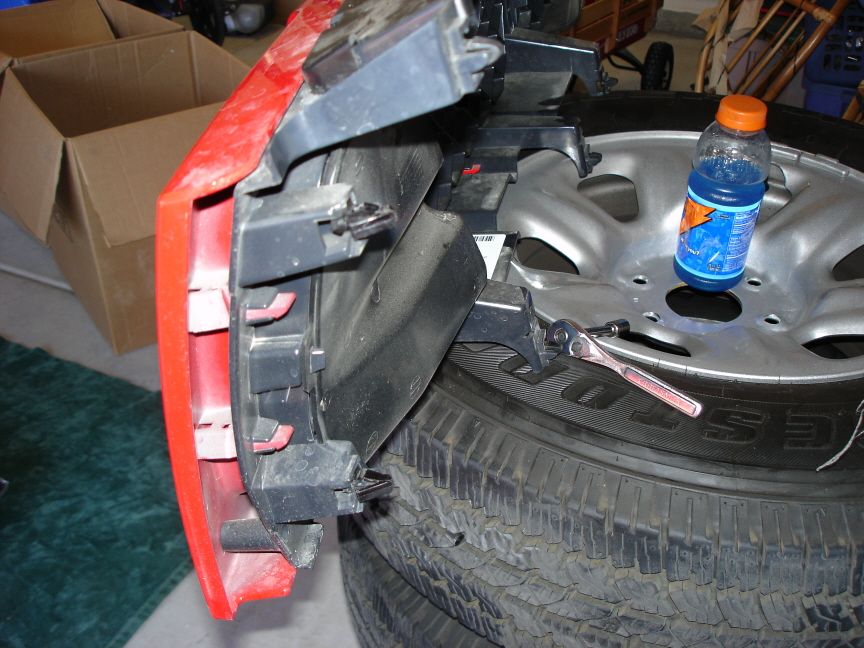 Red bumper cover removed and resting face-down on a spare tire, backing brackets exposed