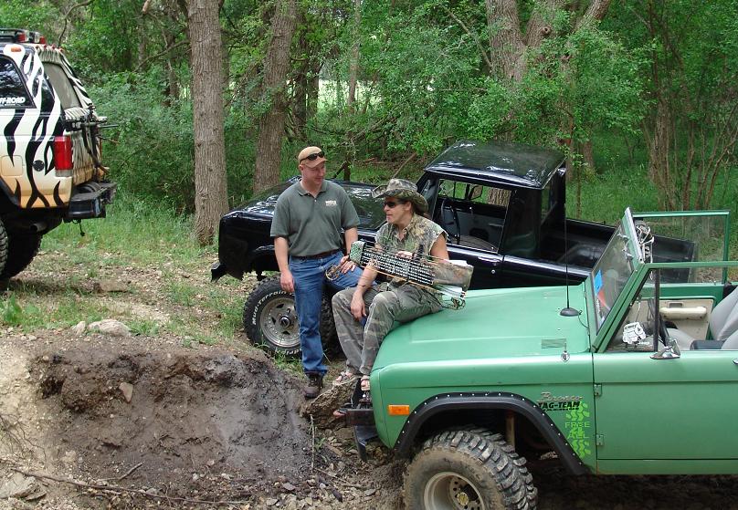 Green Bronco and black pickup truck parked in woods, two people standing nearby