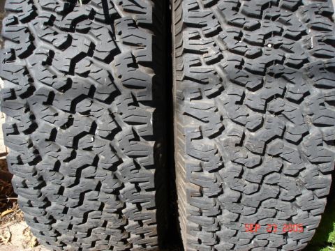 2005 Nissan Titan - Close-up view of two off-road tires, showing their aggressive tread. A watermark indicates 'SUPER MOTORS'.