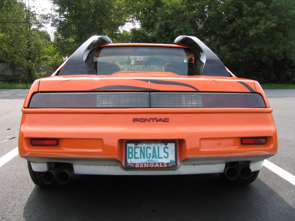 Rear view of orange 1984 Pontiac Fiero with black tiger stripe decals and dual exhaust pipes