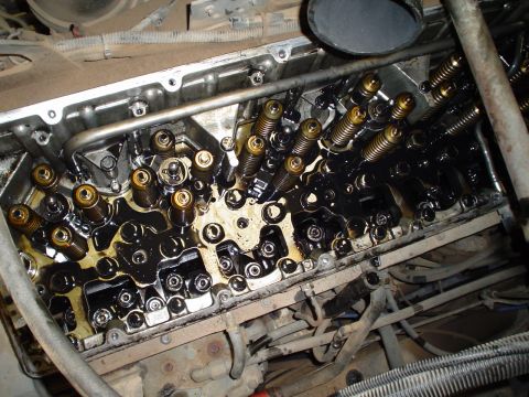 1966 International School Bus - Close-up of an engine's internal components, revealing the valve train mechanism covered in oil.