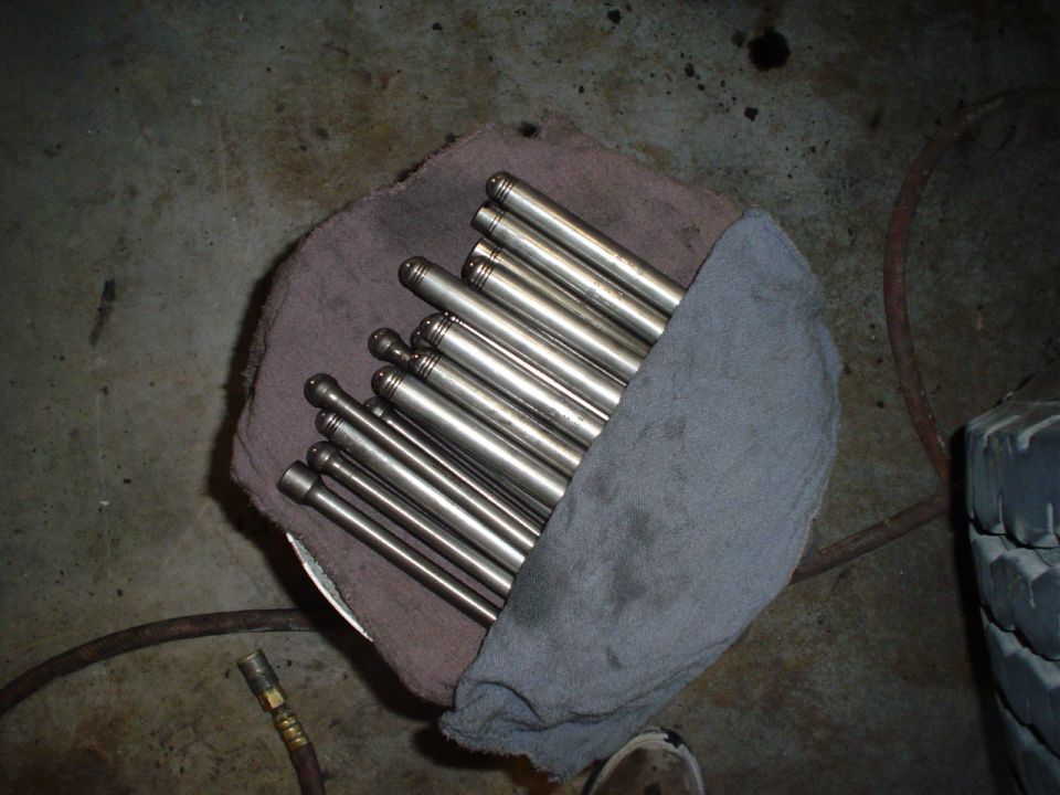 Row of metal engine pushrods on cloth on a garage floor