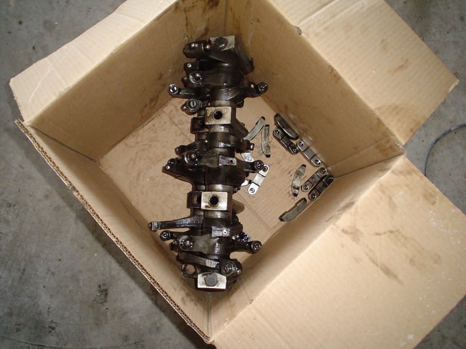 Oily cylinder head with rocker arm assembly in a cardboard box on concrete