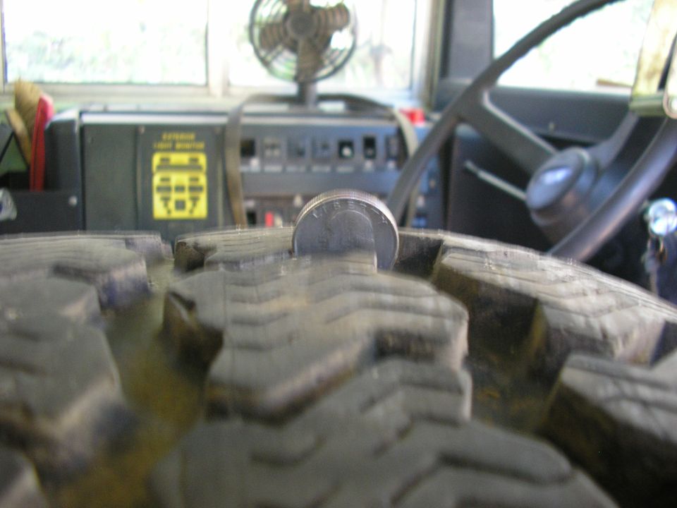Close-up of a tire tread with a coin inserted, showing part of the dashboard and steering wheel