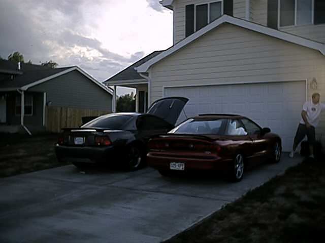 Red sports car with a spoiler and sunroof, license plate 555-SPJ. Black sports car with trunk open