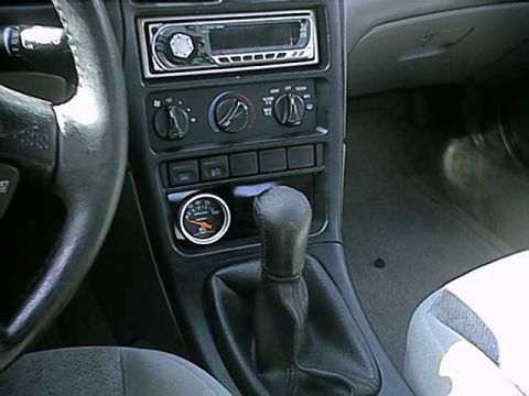 1996 Ford Probe - The interior of a car features a gear shifter, climate controls, and an aftermarket gauge installed on the dashboard.