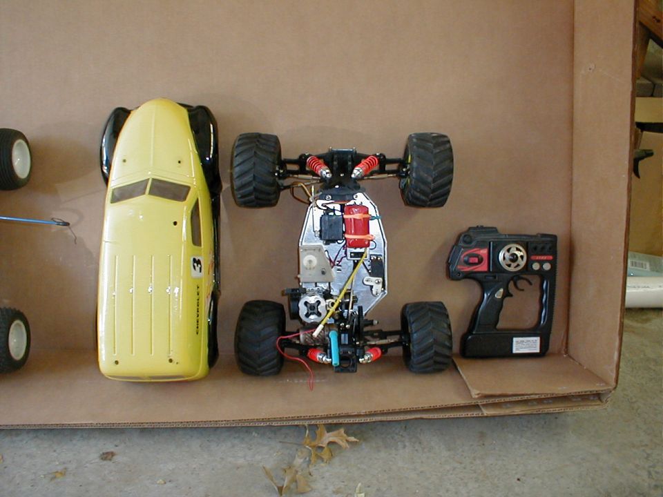 Yellow-bodied nitro RC monster truck and transmitter laid out in a cardboard box