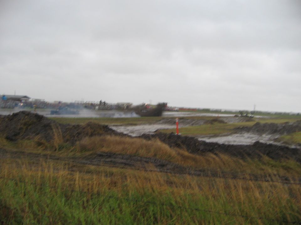 Muddy field with several vehicles in the distance, some kicking up dust