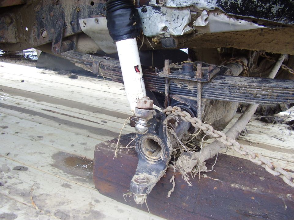 Broken steering knuckle and white shock on muddy leaf-spring front axle