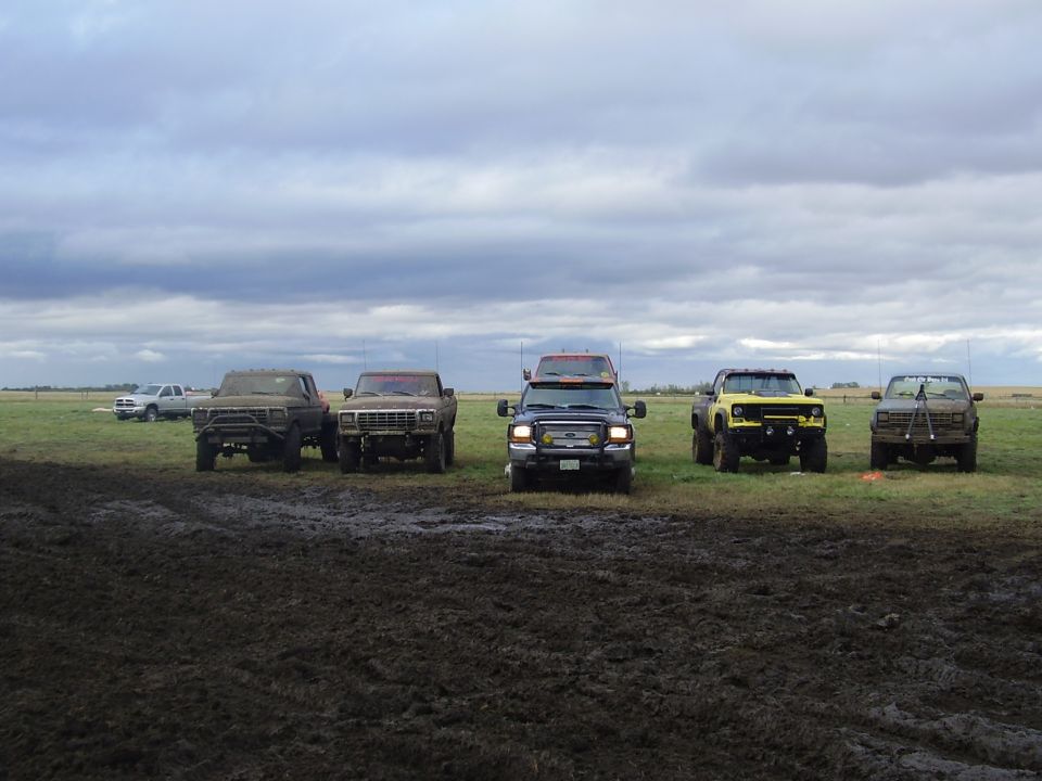 Several pickup trucks parked in a muddy field under a cloudy sky