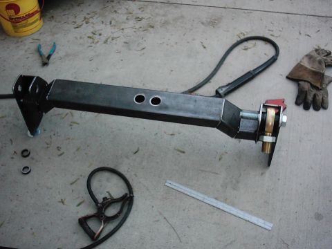 1978 Ford Bronco - A custom-fabricated suspension part sits on a concrete surface, surrounded by welding tools and a yellow bucket.