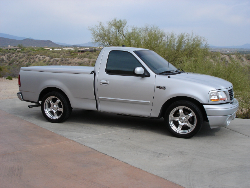 Silver Ford F-150 regular cab pickup, 3/4 front view, chrome wheels, desert backdrop