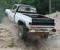 1977 Ford F-150 - White pickup truck navigates a dirt hill, rear view shows off-road tires and suspension.