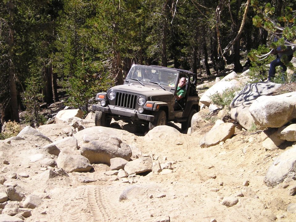 Tan Jeep Wrangler navigating a rocky, off-road trail