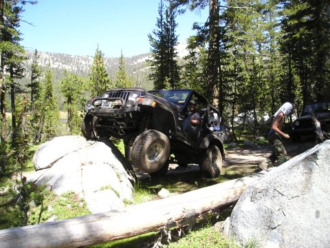 1989 Ford Bronco - Off-road vehicles navigate a rocky trail with a fallen log in the foreground.