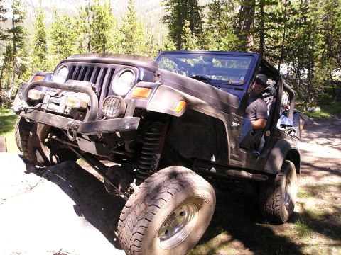 1989 Ford Bronco - A dark Jeep Wrangler navigates a challenging rocky terrain on an off-road trail.