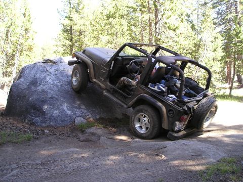 1989 Ford Bronco - Jeep Wrangler TJ navigating an obstacle on a wooded trail.