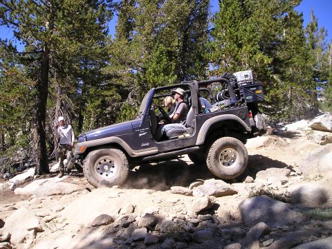 1989 Ford Bronco - A Jeep Wrangler TJ navigates a challenging rocky terrain on a sunny day, surrounded by trees.