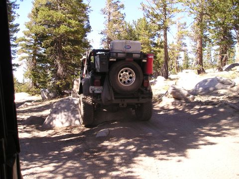 1989 Ford Bronco - Jeep Wrangler navigating a rocky, wooded trail during an off-road excursion.