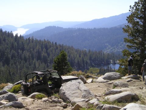 1989 Ford Bronco - A black topless, doorless Jeep Wrangler with a roll bar and rear-mounted spare tire sits parked among granite boulders on a high mountain t…
