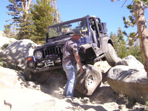 1989 Ford Bronco - A man stands next to a dark blue Jeep Wrangler navigating a challenging rocky trail.