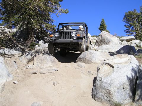 1989 Ford Bronco - Jeep Wrangler TJ off-roading on a sunny day, climbing over large rocks.