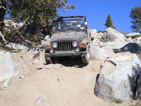 1989 Ford Bronco - A Jeep Wrangler TJ navigates a rocky off-road trail under a clear blue sky.
