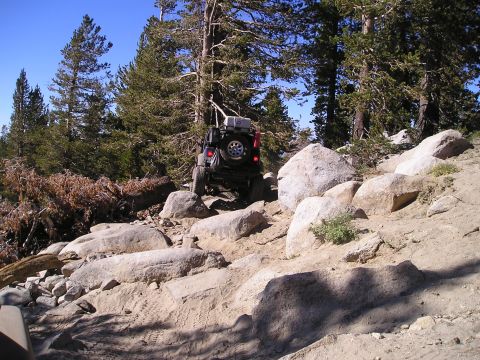 1989 Ford Bronco - Off-road vehicle navigating a challenging rocky terrain in a wooded mountain area.